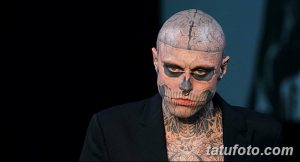 Фото тату: лицо мужчины покрыто татуировкой в виде черепа, выполненной в черно-серых тонах. Взгляд мужчины пронзительный и мрачный.